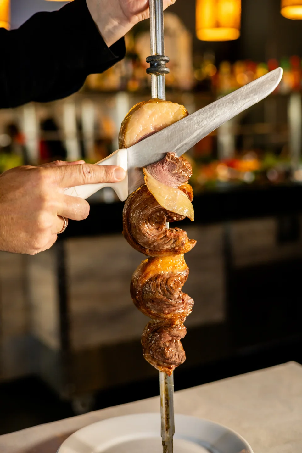 Passador fatiando carne no espeto, com o salão ao fundo
